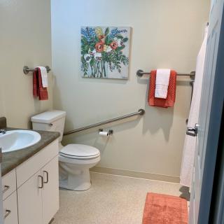 A modern bathroom with a toilet, sink, and shower, featuring colorful towels and artwork on the wall.