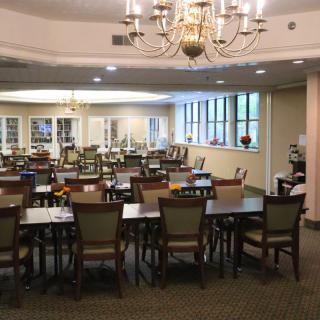 An elegant dining area with multiple tables and chairs, illuminated by chandeliers.