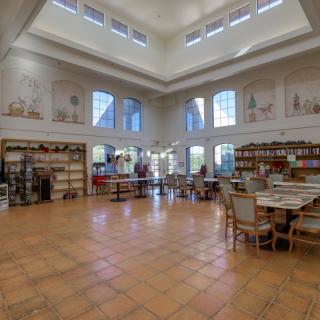 A spacious library interior featuring large windows, bookshelves, and a comfortable reading area.