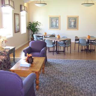 A cozy seating area with purple chairs and wooden tables, decorated with framed art and plants.