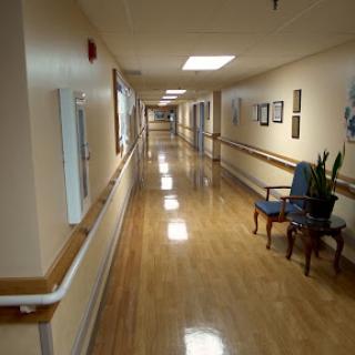 A well-lit hospital hallway featuring polished floors and a few pieces of furniture.