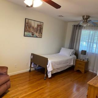 A cozy bedroom featuring a single bed with white linens, a wooden nightstand, and a ceiling fan.