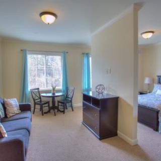 A cozy living space with a dining table, sofa, and an adjacent bedroom, illuminated by natural light through the windows.