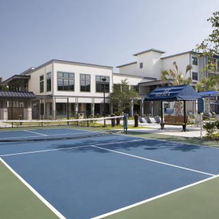 A tennis court in front of a modern residential building on a sunny day.