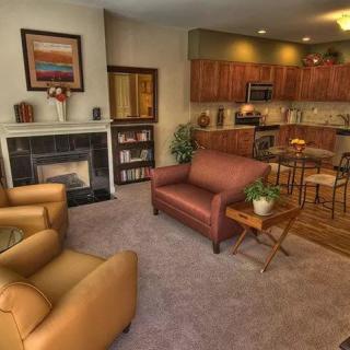 A cozy living room with a fireplace, comfortable seating, and an open view into the kitchen.