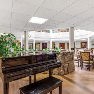 A spacious lobby area with a piano, surrounded by chairs, tables, and greenery.