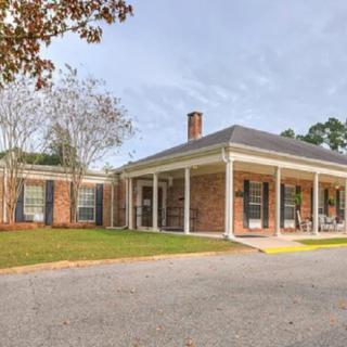 A brick house with a covered porch and a driveway, surrounded by trees.