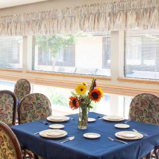 A dining table set with plates and a vase of sunflowers, bathed in natural light.