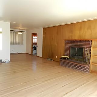 A spacious living room featuring hardwood floors and a brick fireplace with wood paneling.