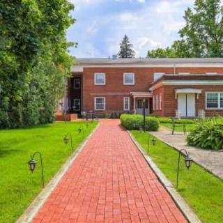 A brick house with a red pathway leading through a green lawn under a sunny sky.