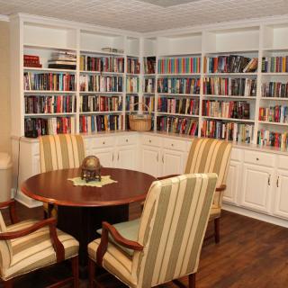 A cozy study room with bookshelves full of books, a round table, and comfortable chairs.