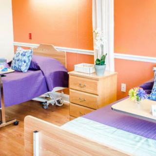 A well-lit hospital room with two beds, featuring purple bedding and an orange accent wall.