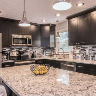 A modern kitchen with granite countertops and dark cabinets, equipped with stainless steel appliances and stylish pendant lighting.