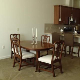 A dining area with a wooden table and chairs, adjacent to a kitchen with bar seating.