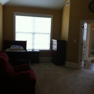 A well-lit room with furniture, including a bed, dresser, and armchair.
