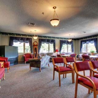 A cozy living room with multiple seating areas, featuring red chairs and large windows.