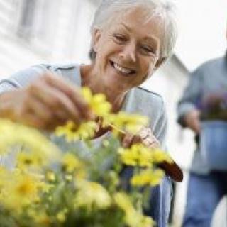 An elderly woman happily tending to flowers in her garden.