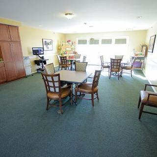A spacious room with tables, chairs, and large windows allowing natural light.