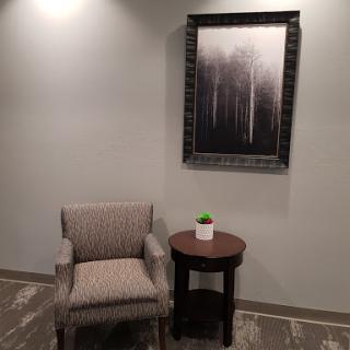 A cozy corner featuring a patterned chair and a small table with a plant, complemented by abstract artwork on the wall.