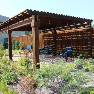 A wooden pergola with outdoor seating set in a landscaped garden area.