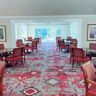 A bright dining area with red and patterned carpet, featuring multiple tables and chairs.