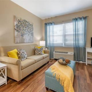 A cozy living room with a beige sofa, colorful pillows, and a stylish coffee table, illuminated by natural light streaming through sheer curtains.