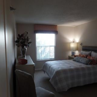 A cozy bedroom with a neatly made bed, side table lamp, and window with curtains.