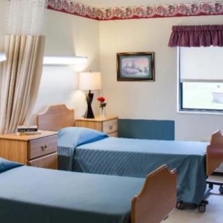 A hospital room with two beds, a small table, and a lamp.