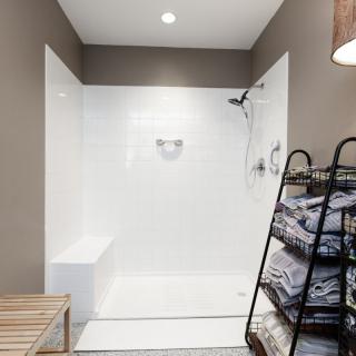 A modern and minimalist bathroom featuring a walk-in shower, neatly folded towels on a storage rack, and a wooden bench.