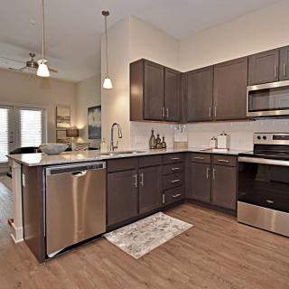 A modern kitchen featuring stainless steel appliances and wooden cabinets, with an open plan design that emphasizes natural light.