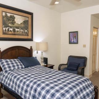 A cozy bedroom featuring a plaid-patterned bed, an armchair, and paintings on the wall.