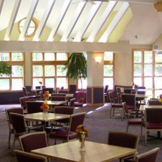A spacious dining area with tables and chairs, illuminated by natural sunlight through large windows.