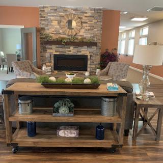 A cozy and inviting living room featuring a stylish wooden console table, decorative plants, and a warm stone fireplace.