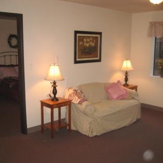 A cozy living room with a sofa, side tables, and lamps, featuring a piece of artwork on the wall.