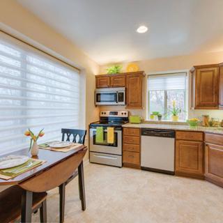 A modern kitchen with wooden cabinets and stainless steel appliances, featuring a cozy dining area illuminated by natural light.