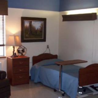 A hospital room featuring a medical bed, side table with a lamp, and a window with blinds.