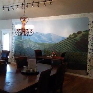 A dining room featuring a large mural of a vineyard landscape and a decorative chandelier.