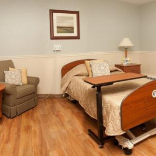 A clean and organized hospital room with a comfortable bed, cushioned chair, and wooden flooring.