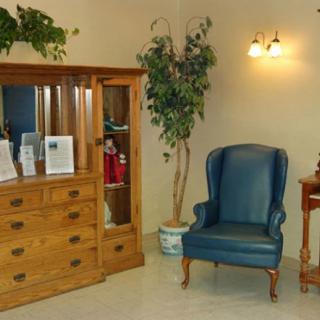 A cozy living room corner featuring a blue armchair, wooden cabinet, and potted plant under warm lighting.