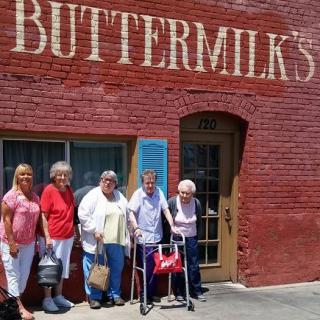 A group of people standing outside a brick building with the sign 'BUTTERMILK'S'.
