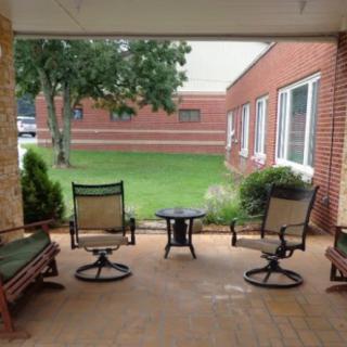 A cozy patio with chairs and a table, overlooking a garden and brick building.