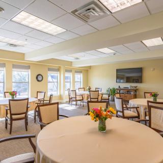 A well-lit indoor dining area with neatly arranged tables and chairs, decorated with flowers.