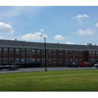 A brick school building with a parking lot and cloudy sky.