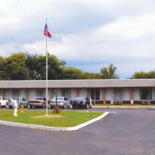 A view of a motel with an American flag and parked cars under a cloudy sky.