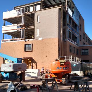 A building under construction with scaffolding and cranes on a sunny day.