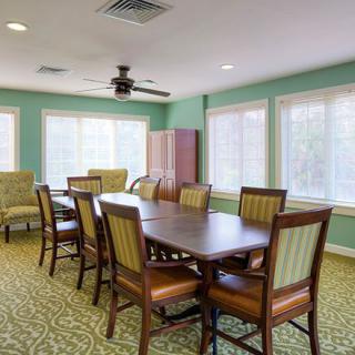 A bright dining room with a large table and chairs, featuring green walls and ample natural light through multiple windows.