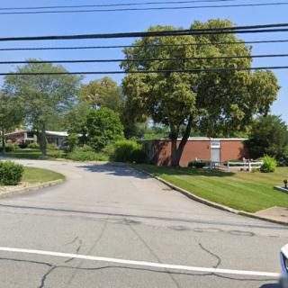A street intersection with overhead power lines, surrounded by trees and a small brick building.