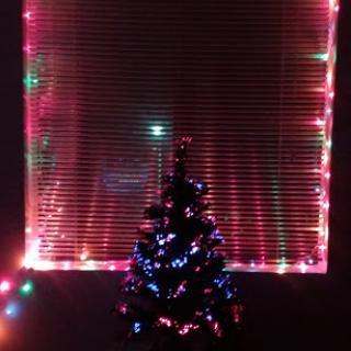 A beautifully decorated Christmas tree illuminated by colorful lights, set against a backdrop of festive window decorations.