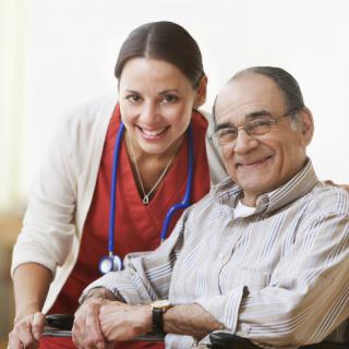 A nurse smiling while assisting an elderly man in a wheelchair.
