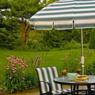 A cozy patio setup with a striped umbrella, surrounded by lush greenery and vibrant flowers.